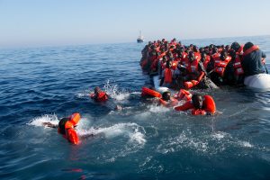 Flüchtlinge schwimmen im Wasser vor einem sinkenden Schlauchboo